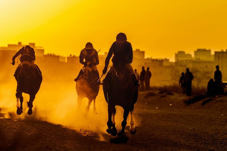 Arabian horses racing at full speed during sunset, creating a dramatic scene with dust